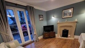 A living room with a sofa, television, fireplace, and a view through a glass door. - Three Farthings Bed & Breakfast, a quiet and peaceful countryside location. (Driffield)