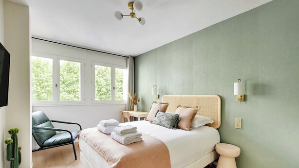 A bedroom with a bed, bedside table, chair, and a small potted plant. - Modern "Green Suites" residence - Meudon/Vélizy (Meudon)