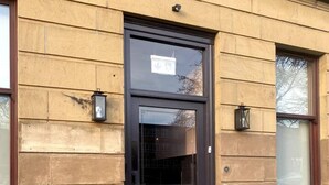 Un edificio con puerta oscura, dos faroles de pared y un ventanal con vidrio esmerilado.