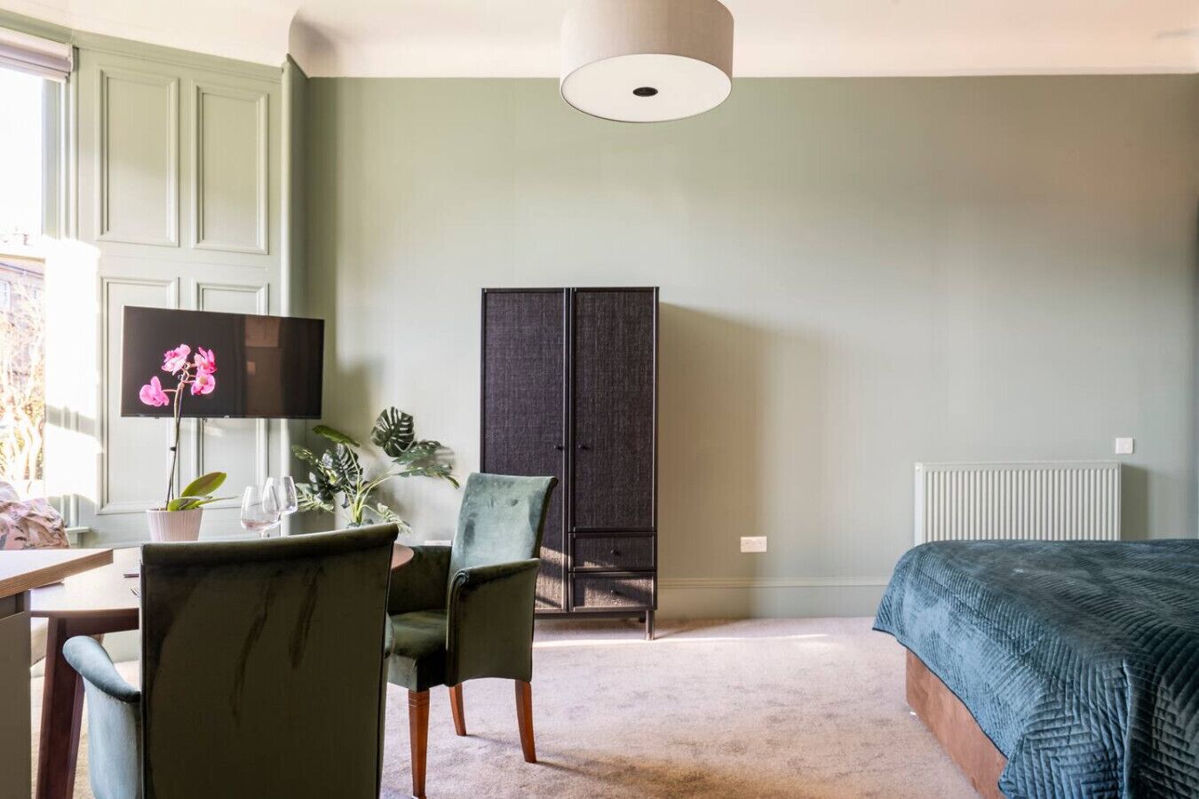 A bedroom with a bed, a desk with a chair, a cabinet, and a window with curtains.