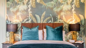 Un dormitorio con una cama, dos mesitas de noche y una pared decorada con un mural de plantas tropicales.