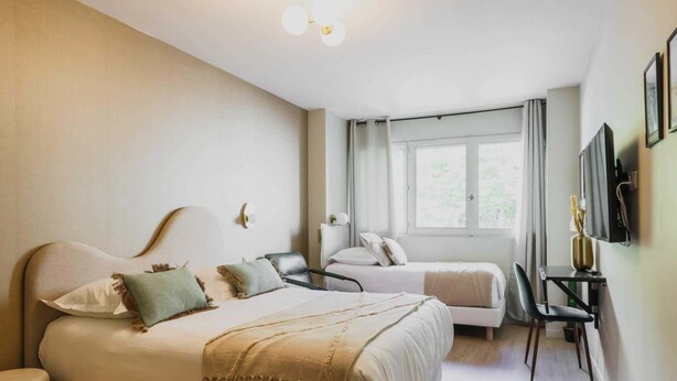 A hotel room with a large bed, a smaller bed, a desk, and a chair. There is a window with curtains and a flat-screen TV mounted on the wall. - Modern "Green Suites" residence - Meudon/Vélizy (Meudon)