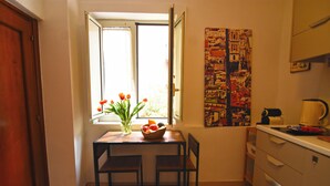 A small kitchen with a table and chairs, a window with a view, and a wall with a cityscape print. - La Casa di Apollo (Naples)