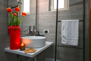 A modern bathroom with a white sink, red vase with tulips, a lit candle, and a towel rack. - La Casa di Apollo (Naples)