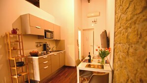 A compact kitchen with wooden flooring, a white dining table, and a small seating area. - La Casa di Apollo (Naples)