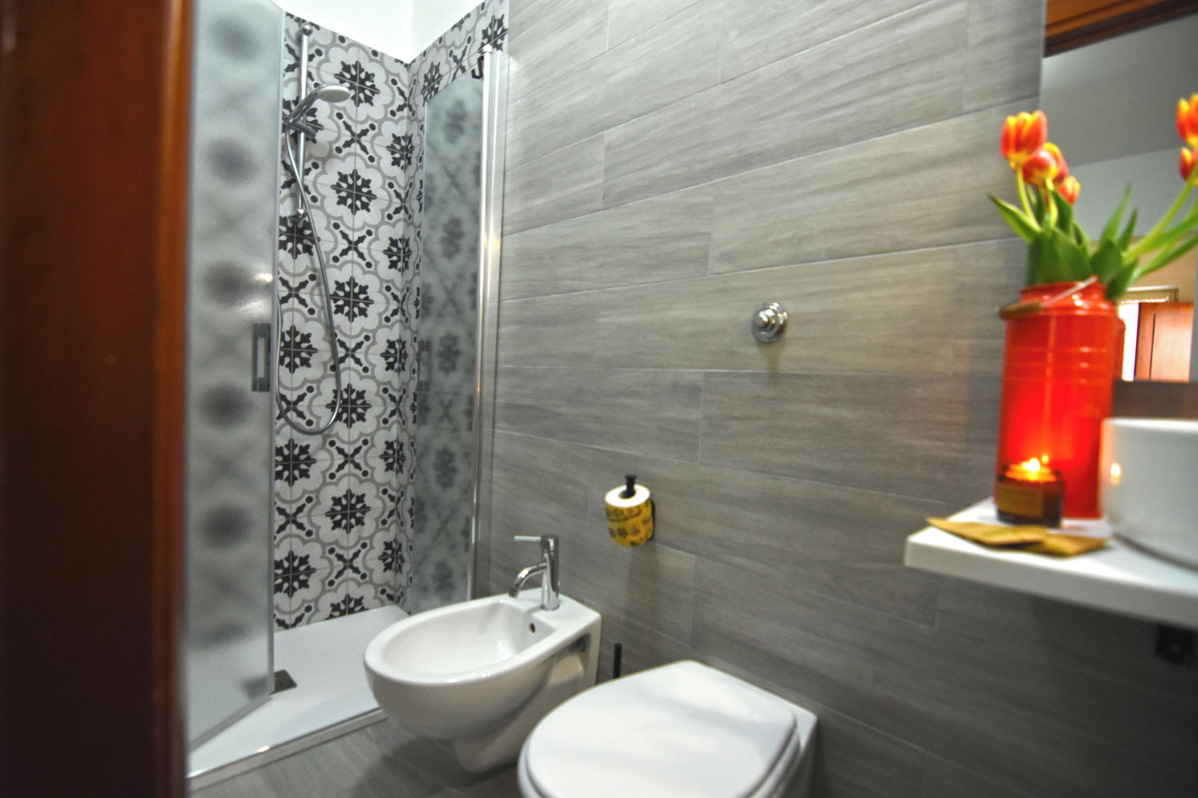 Un baño con ducha, bidé, inodoro y una repisa con un jarrón de flores.