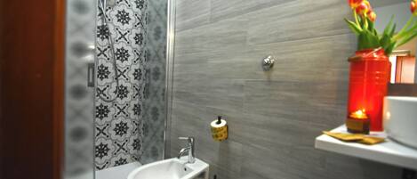 Un baño con ducha, bidé, inodoro y una repisa con un jarrón de flores.