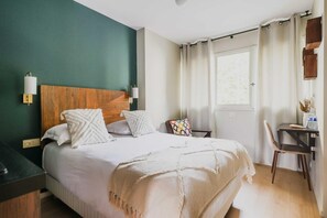 Une chambre bien rangée, avec un lit, une table de chevet, une chaise et une fenêtre avec des rideaux.