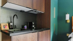 Een kleine keuken met een modern design, voorzien van een zwarte spoelbak, een roestvrijstalen kraan en een inbouwafzuigkap.
