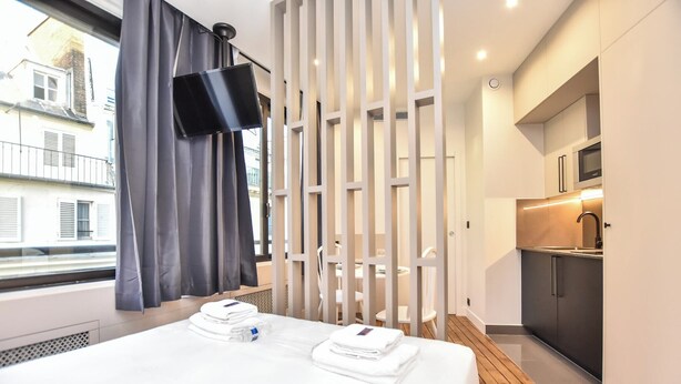 A modern hotel room with a neatly made bed, a television mounted on the wall, and a kitchenette area. - Magnificent studio - 2P - near the Palais Garnier (Paris)