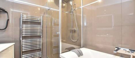 A modern bathroom with a glass-enclosed shower, a chrome towel rack, and a white bathtub.