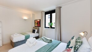 Habitación de hotel con dos camas, una ventana con cortinas, una lámpara de pared y un cuadro.