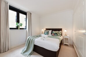 Un dormitorio ordenado con cama, mesitas de noche y una ventana con cortinas.