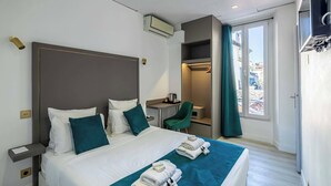 A hotel room with a large bed, a desk, a chair, and a view of the city through the window.