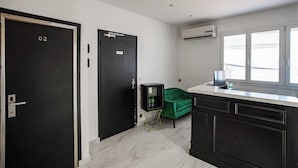 A room with a black door labeled "02", a green sofa, a small black cabinet, and a window with blinds.