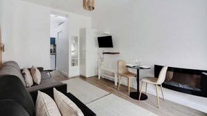 A modern living room with a sofa, a fireplace, a dining table with chairs, and a flat-screen TV mounted on the wall. - Magnificent studio - 2P - Near Bastille (Paris)