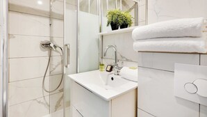 A modern bathroom with a glass shower enclosure, a white sink with a marble countertop, and a mirror above the sink. - Magnificent studio - 2P - Near Bastille (Paris)