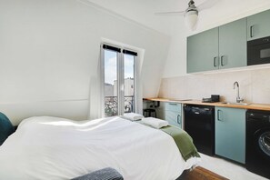 A compact bedroom with a bed, a small kitchenette, and a window with curtains.