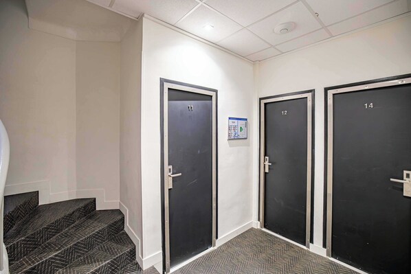 Un pasillo con tres puertas, numeradas 12, 13 y 14, que dan a habitaciones. Hay un cartelito en la pared entre las puertas 12 y 13.