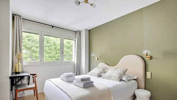 A bedroom with a bed, a desk, a chair, a window, and a wall-mounted light fixture. - Modern "Green Suites" residence - Meudon/Vélizy (Meudon)