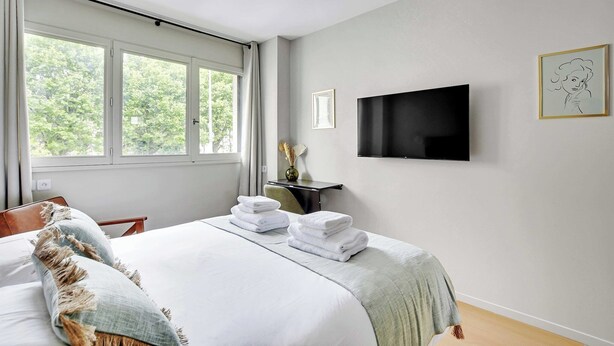 A bedroom with a bed, a TV mounted on the wall, and a window with curtains. - Modern "Green Suites" residence - Meudon/Vélizy (Meudon)