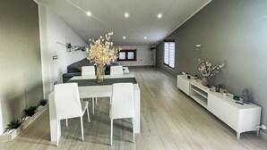 A modern living room with a dining area, featuring a white sofa set, a dining table with chairs, and a vase with flowers.