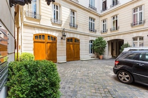 Enter a charming courtyard with a cobblestone floor, flanked by two entrance doors and a lush potted plant.