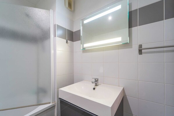 Une salle de bain moderne avec une douche à parois de verre, un lavabo blanc avec un miroir au-dessus et un porte-serviettes.