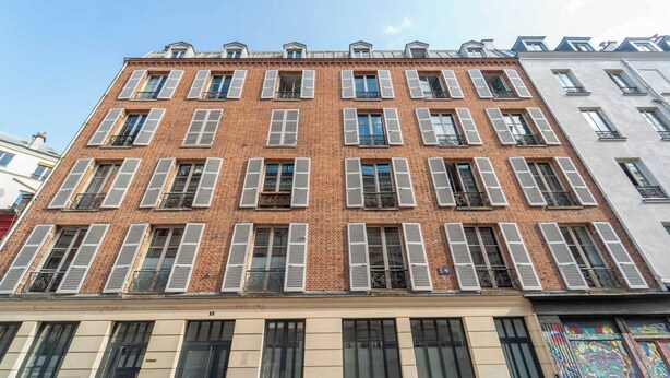 Un edificio de varios pisos con fachada de ladrillo, contraventanas blancas y varios balcones.
