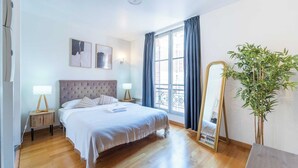Un dormitorio con cama, mesitas de noche, un espejo y una planta en maceta.