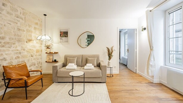 Uma sala de estar moderna com parede de pedra, um sofá, uma poltrona de couro, uma mesa redonda e um lustre.