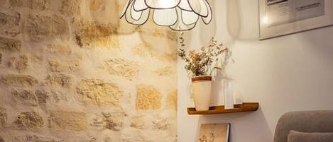 A cozy room with a stone wall, a brown leather chair, a grey sofa, a round white table, and a pendant light.