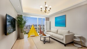 Un salon moderne avec un canapé, une petite table basse, une tente de jeu jaune et une vue sur la ville à travers de grandes fenêtres.