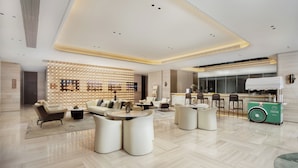Un hall d’hôtel moderne avec un comptoir d’accueil, des espaces de détente et un distributeur automatique de produits écologiques.