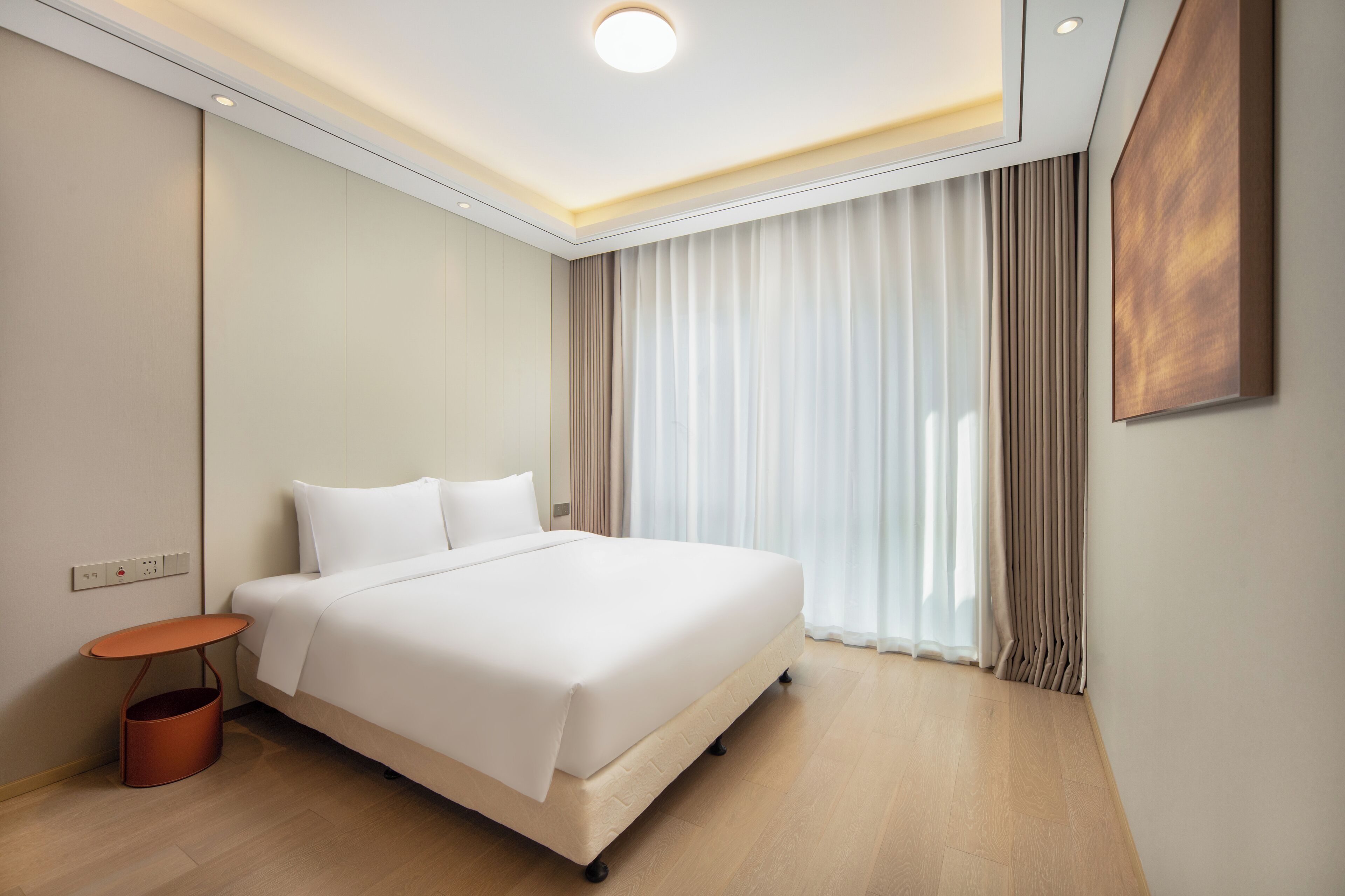 Ein modernes Hotelzimmer mit einem großen Bett, einem kleinen Nachttisch und einem großen Fenster mit Vorhängen.