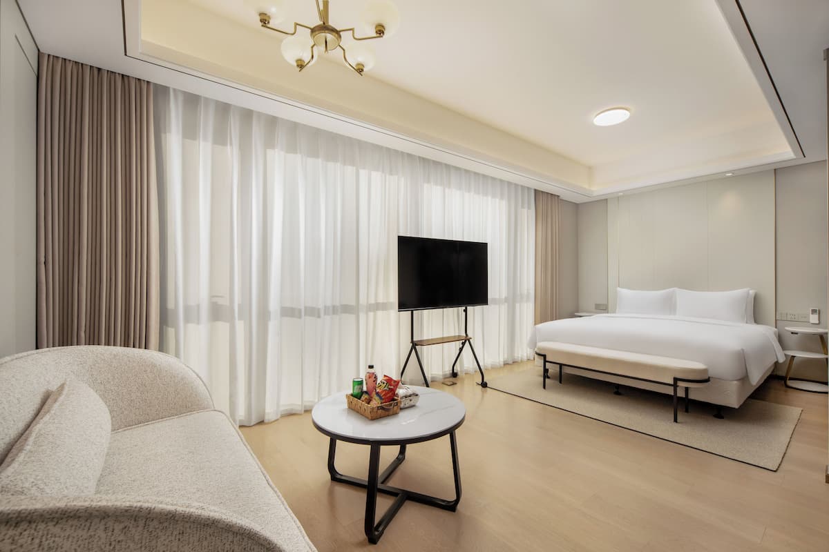 Ein modernes Hotelzimmer mit einem Bett, einem Fernseher, einem kleinen runden Tisch mit Snacks und einer Bank.