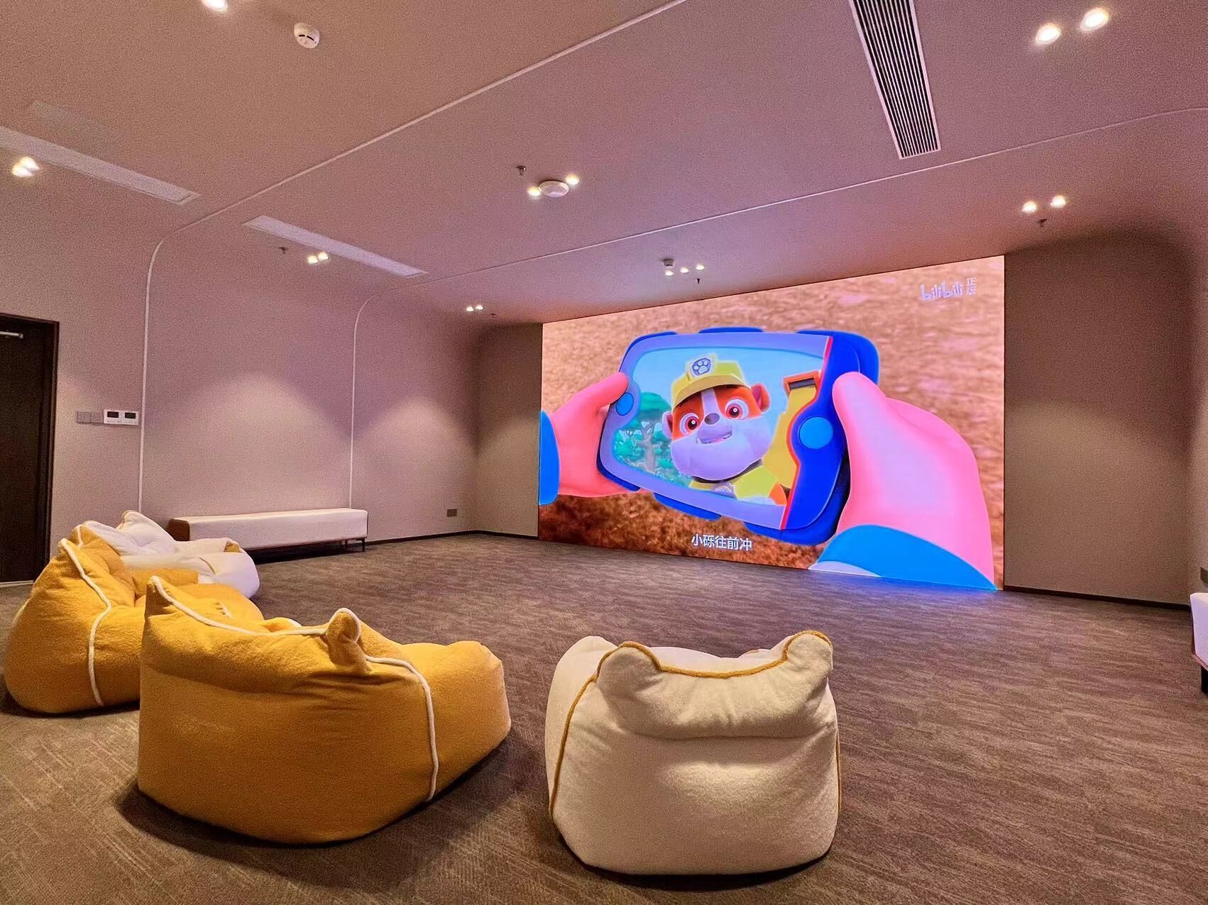 A modern hotel room with a large screen displaying a cartoon character, plush seating, and a minimalist design.