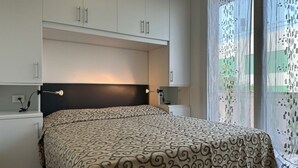 A bedroom with a bed, two bedside tables, a headboard, and a window with patterned curtains.
