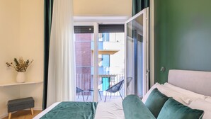 Et soveværelse med en seng, en bænk, en potteplante og udsigt til en balkon med stole og gelænder.