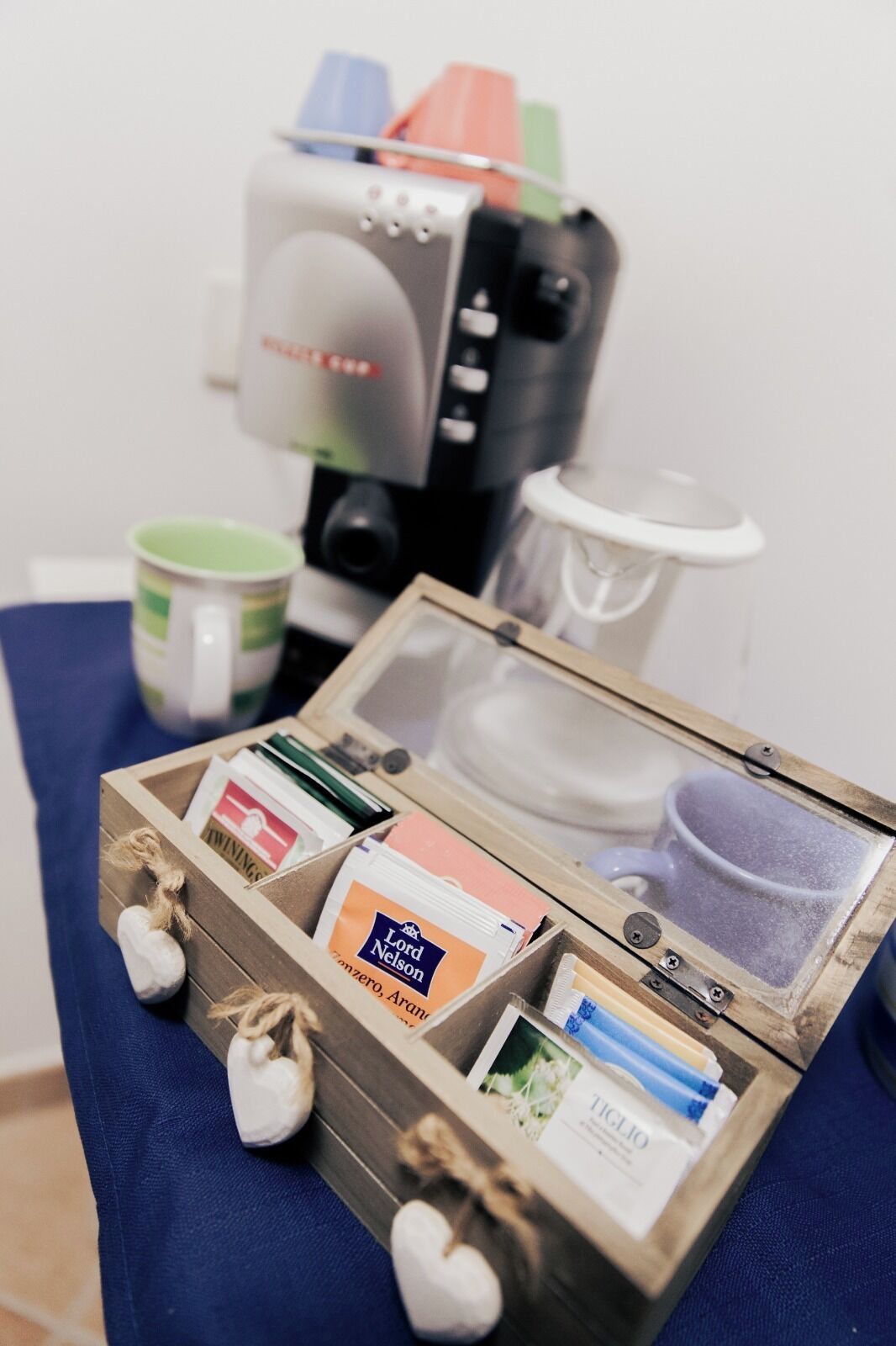 A coffee machine, a wooden box with various items, and a green mug on a blue surface.