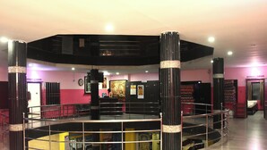A spacious indoor area with a central open space surrounded by black columns, a reception desk, and a staircase leading to an upper level. - Uma Residency (Mayiladuthurai)