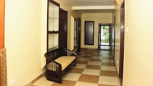 A hallway with a checkered floor, a bench, and a door leading to a garden. - Uma Residency (Mayiladuthurai)