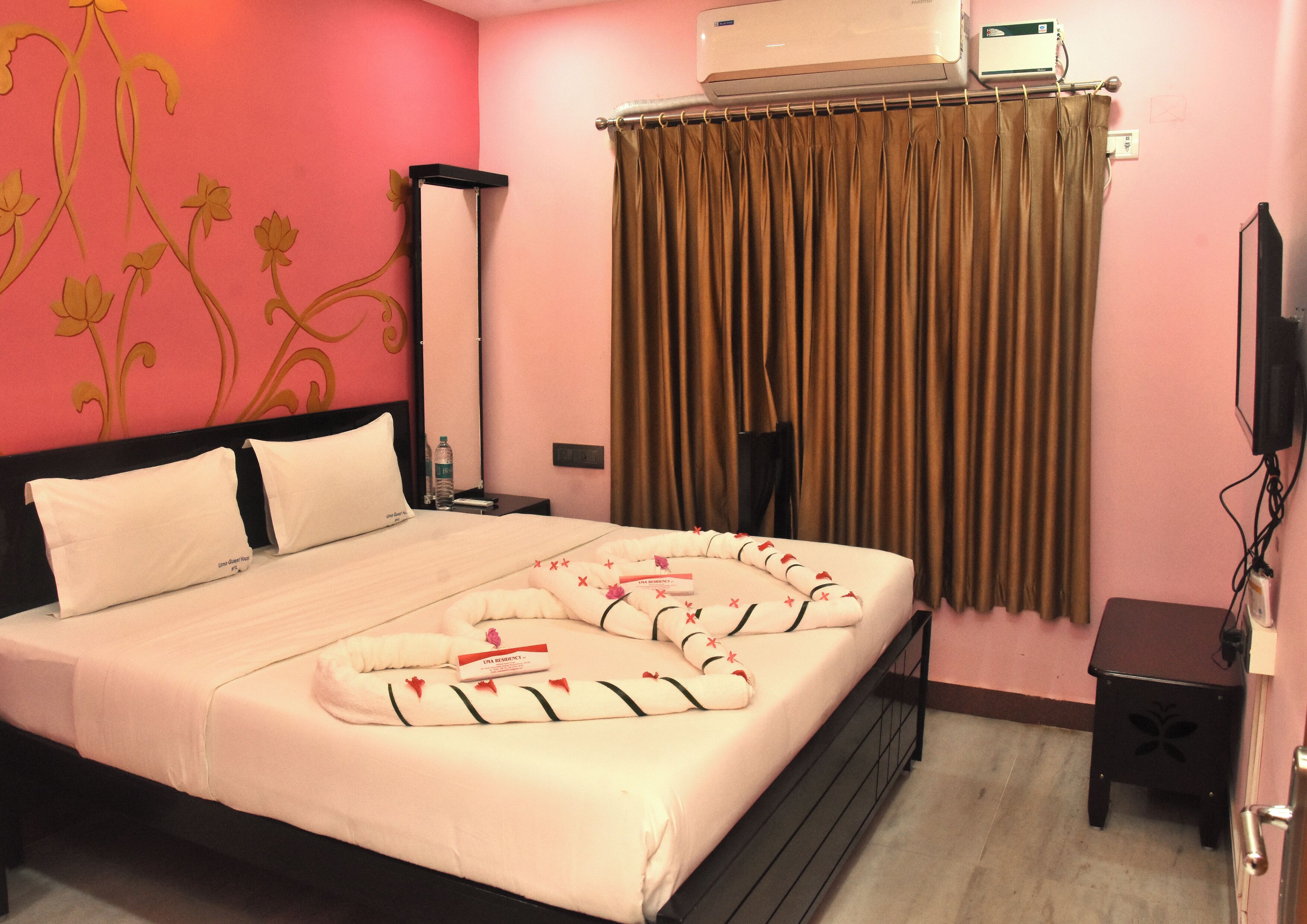 A hotel room with a bed, a nightstand, a TV, and a window with curtains.