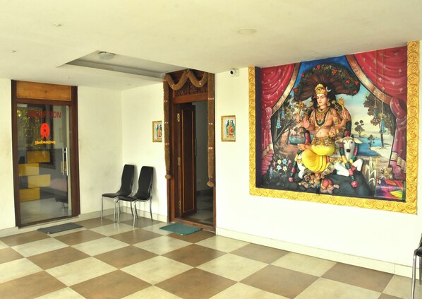 Un área de recepción con suelo a cuadros, dos sillas negras, una mesa de recepción y un mural de una deidad.