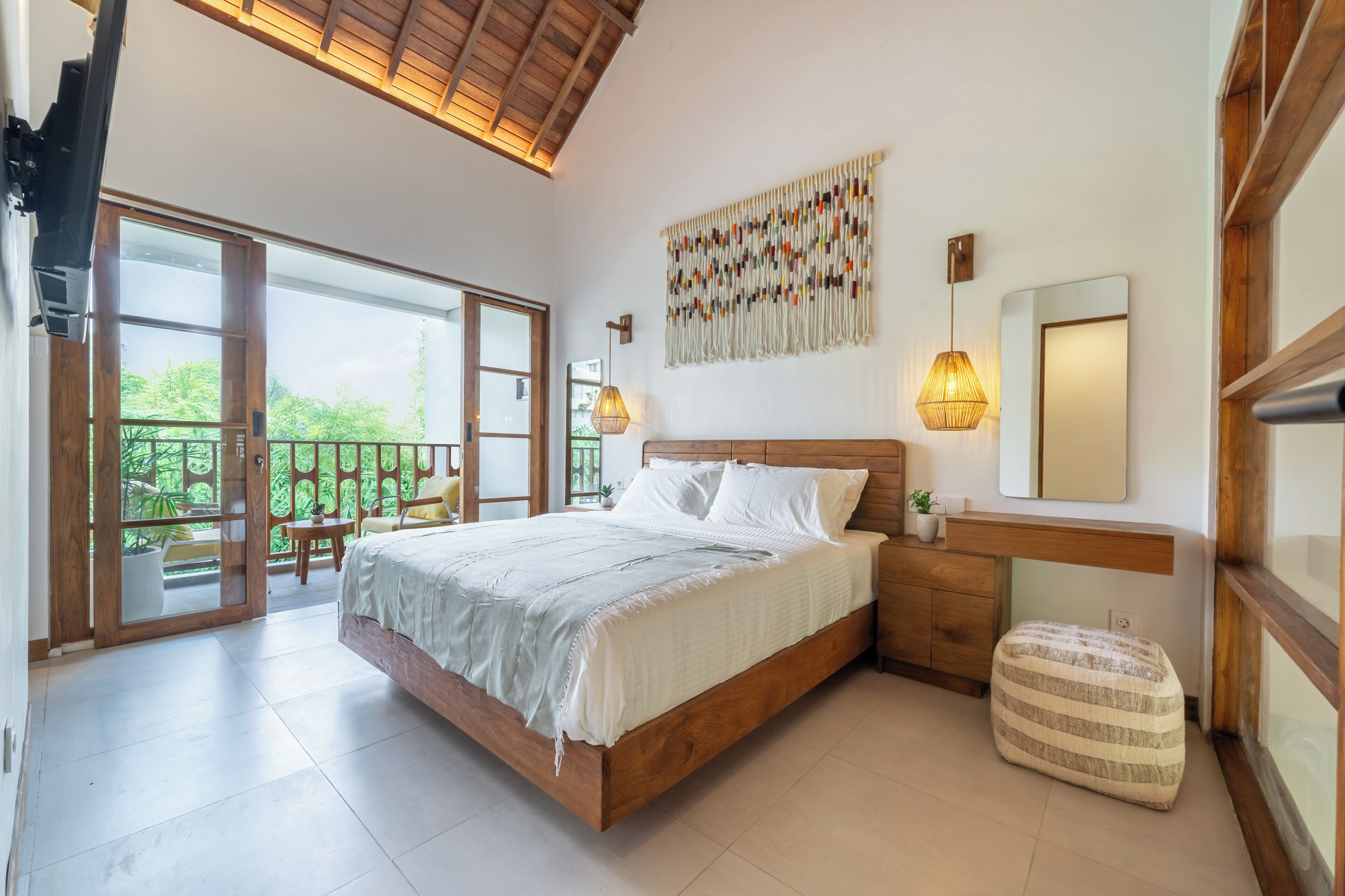 A bedroom with a wooden bed, a large window, a balcony, and a wall-mounted light fixture.