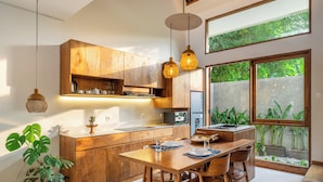 A modern kitchen with wooden cabinetry, a dining table, and pendant lighting. - Chindaga Villa Canggu (Canggu)