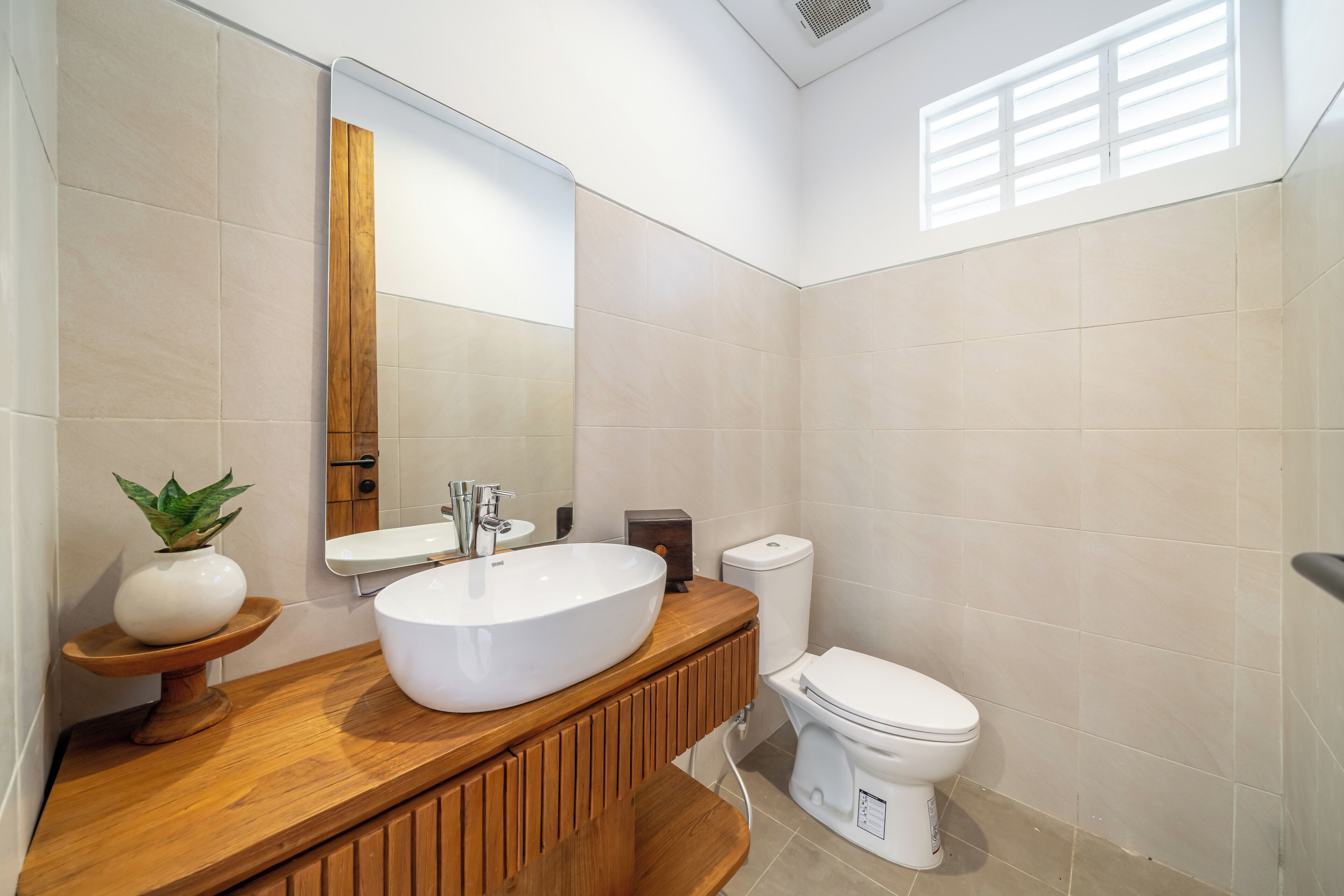 Un baño moderno con tocador de madera, lavamanos blanco y retrete.