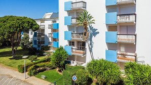 Um edifício residencial com vários andares, varandas, um jardim bem cuidado e um céu azul límpido.