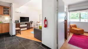 Uma sala de estar moderna com uma TV de tela plana, uma área de refeições com mesa e cadeiras, e uma poltrona laranja aconchegante.