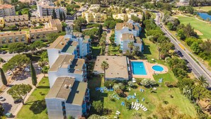 Vista aérea de uma área residencial com vários prédios de apartamentos, uma piscina e um campo de golfe ao fundo.